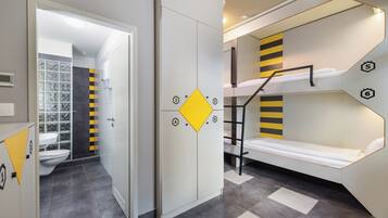 A compact room with a bunk bed, a wardrobe, and a bathroom with a toilet and shower.