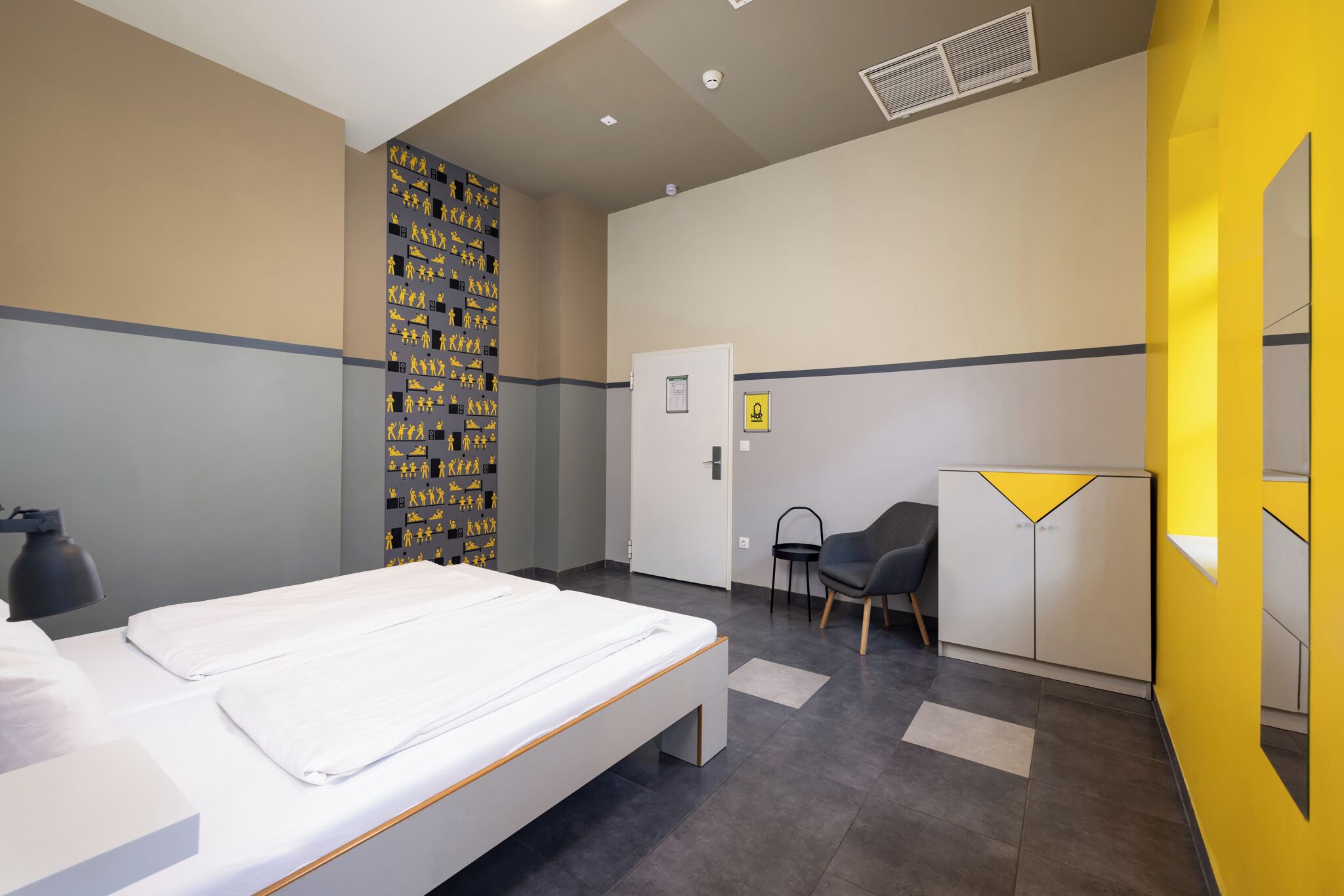 A modern hotel room with a bed, a desk, a chair, and a wardrobe.