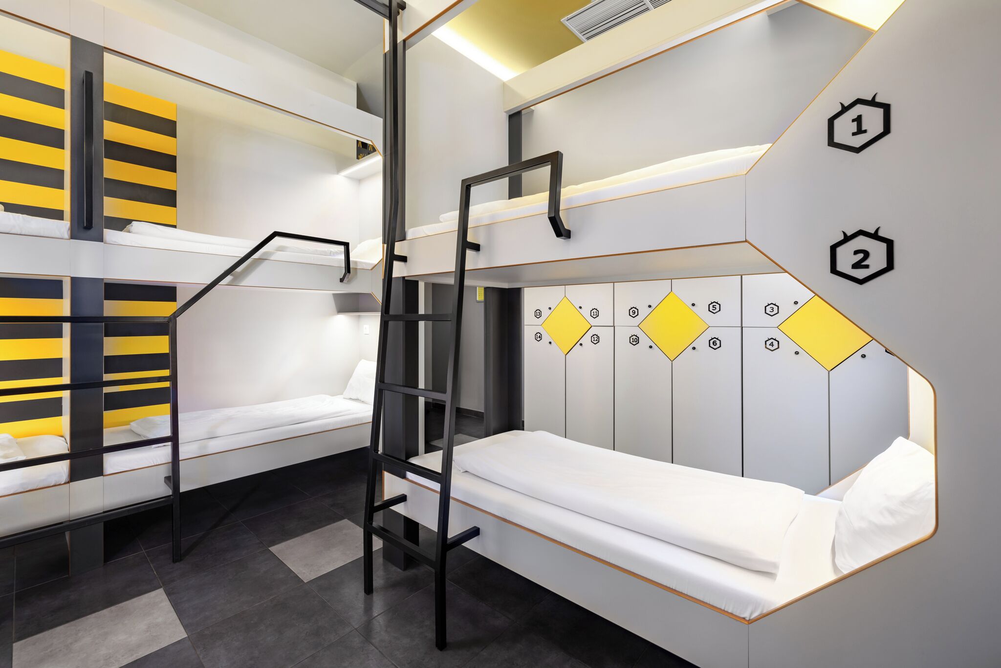 A modern hotel room with bunk beds, a ladder, and a wall with numbered compartments.