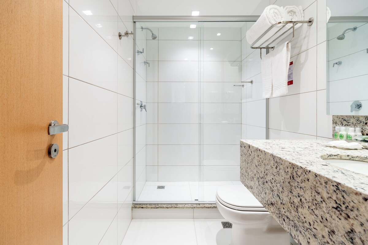 Een moderne badkamer met een douchecabine van glas, een marmeren aanrecht en een toilet.