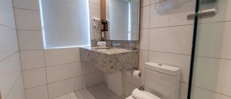 Un baño con inodoro blanco, lavamanos de mármol, espejo y zona de ducha.