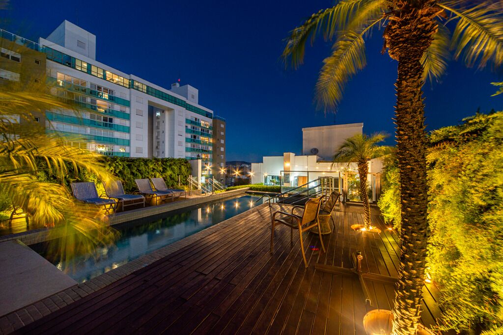 A pool area with lounge chairs, a wooden deck, and a building with multiple floors and balconies.