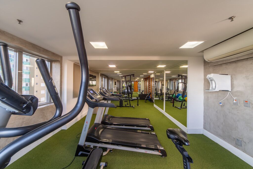 Un gimnasio con cintas de correr, equipo de ejercicio y piso cubierto de moqueta verde.