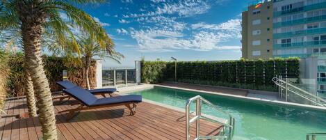 A pool area with wooden deck, lounge chairs, and a palm tree.