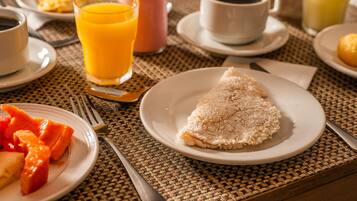 Mesa de café da manhã com pratos de comida, xícara de café e copo de suco de laranja.