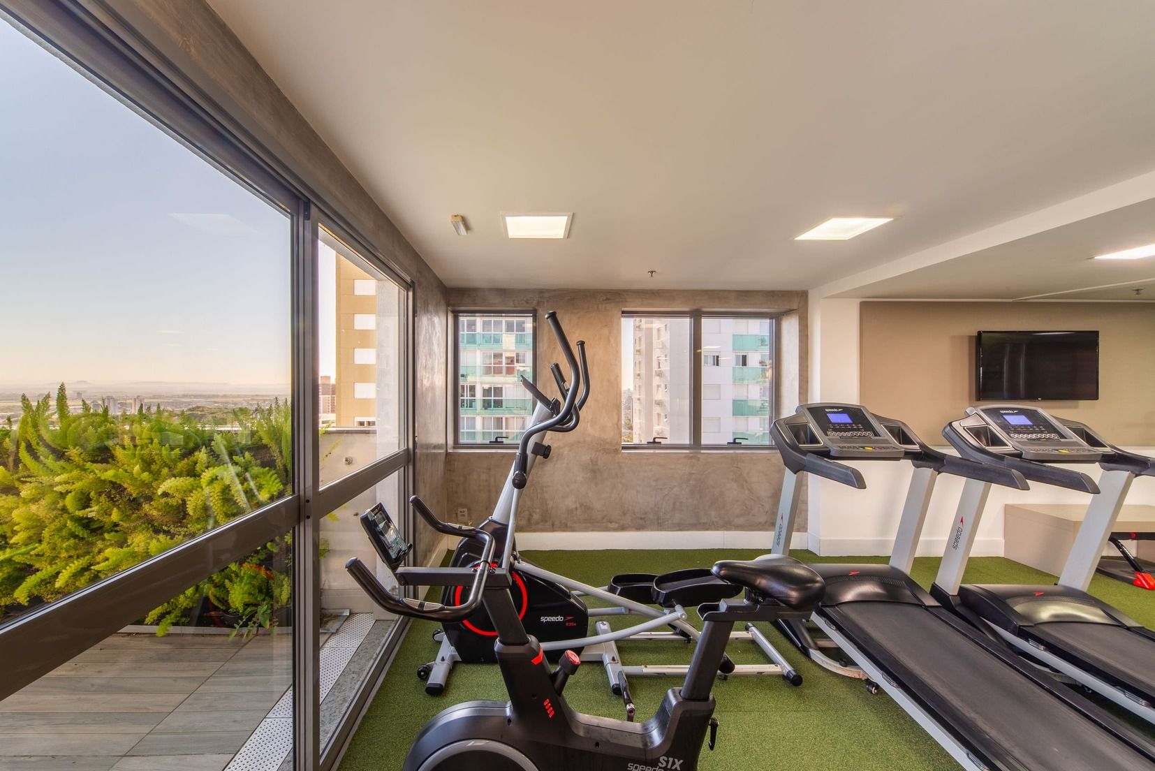 A gym with exercise equipment, a large window, and a view of buildings.