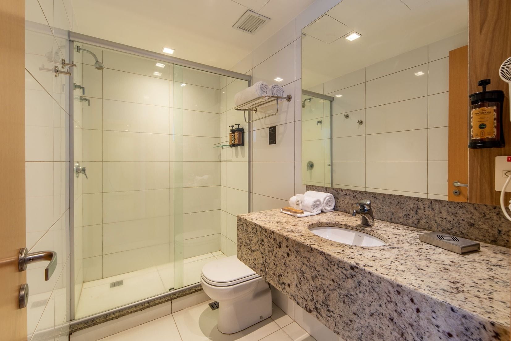 Un baño moderno con cabina de ducha de vidrio, encimera de granito y un espejo grande.