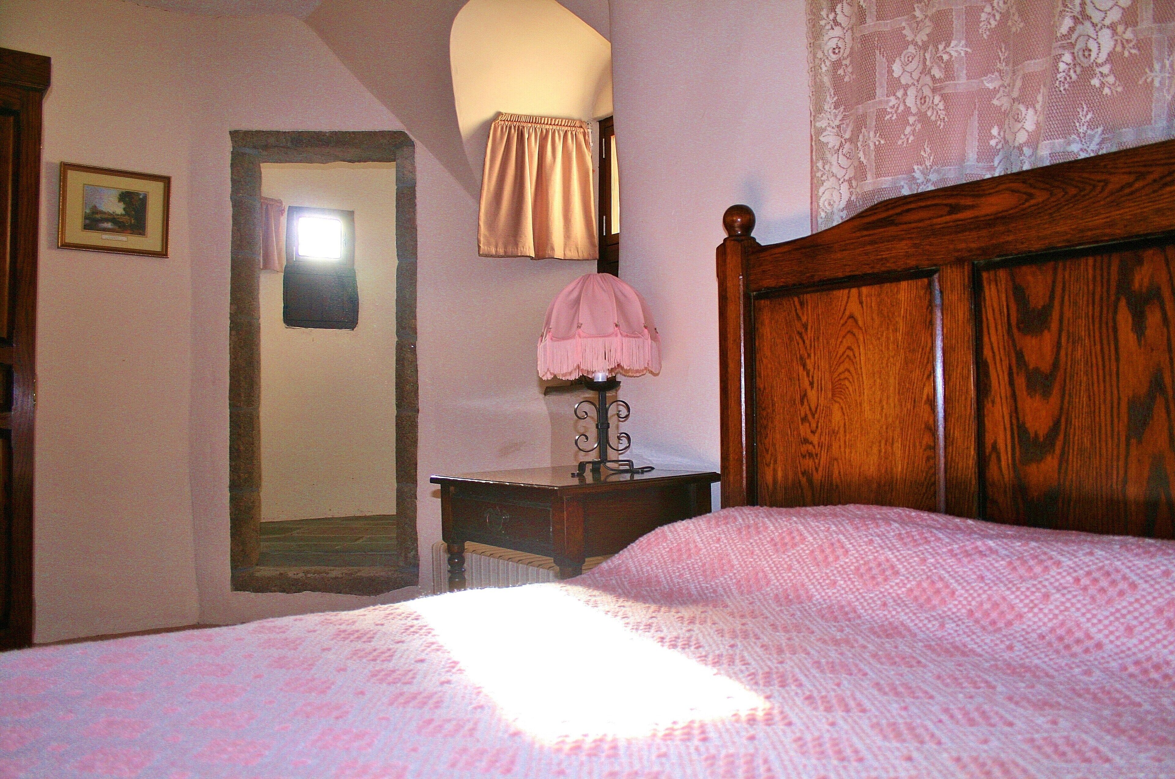 Ein Schlafzimmer mit einem hölzernen Bett, einem Nachttisch mit Lampe, einem Spiegel und einem gerahmten Bild an der Wand.