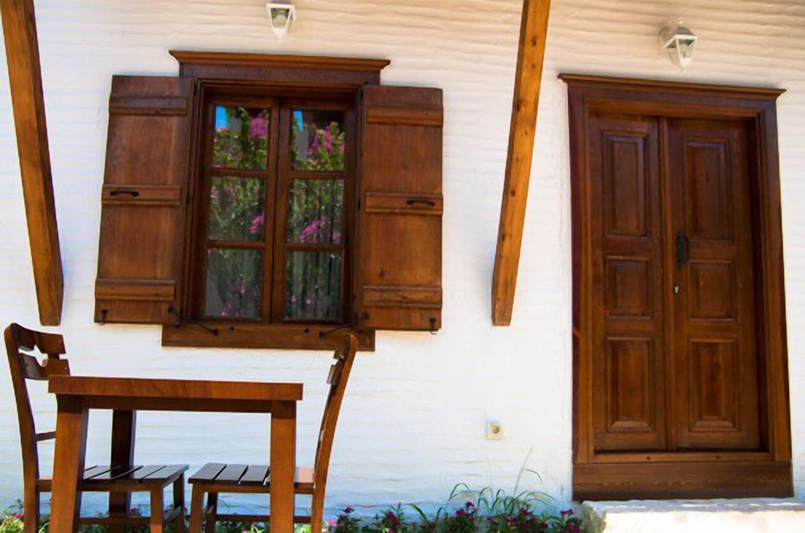 Un bâtiment blanc avec une porte en bois et des volets aux fenêtres, un banc en bois et une petite table.