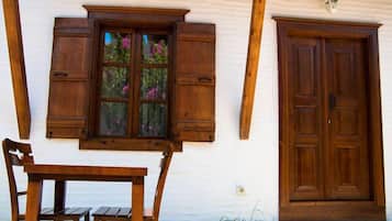 Un bâtiment blanc avec une porte en bois et des volets aux fenêtres, un banc en bois et une petite table.