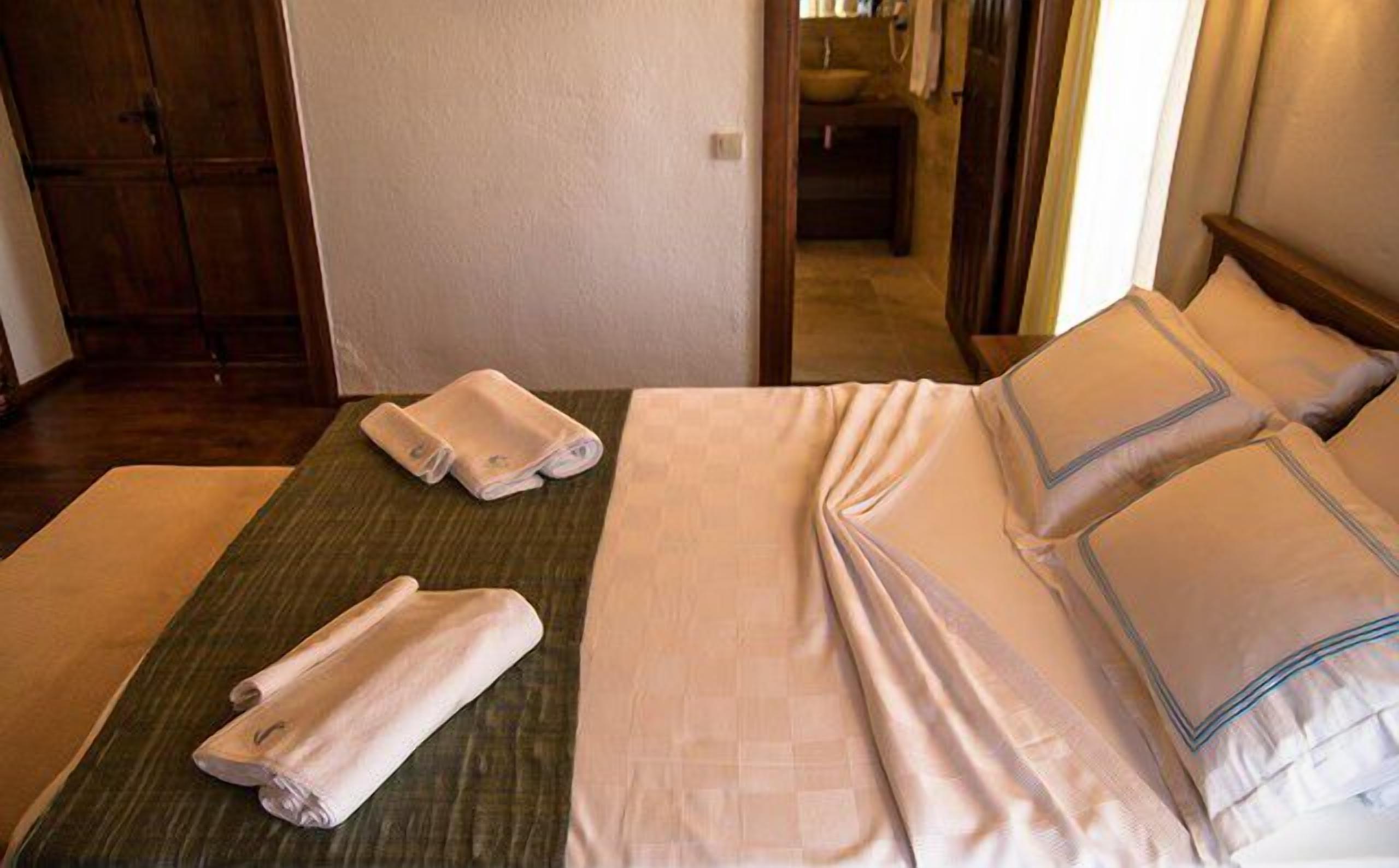 Una cama bien hecha con almohadas y toallas dobladas, suelo de madera y un armario de madera en una habitación de hotel.