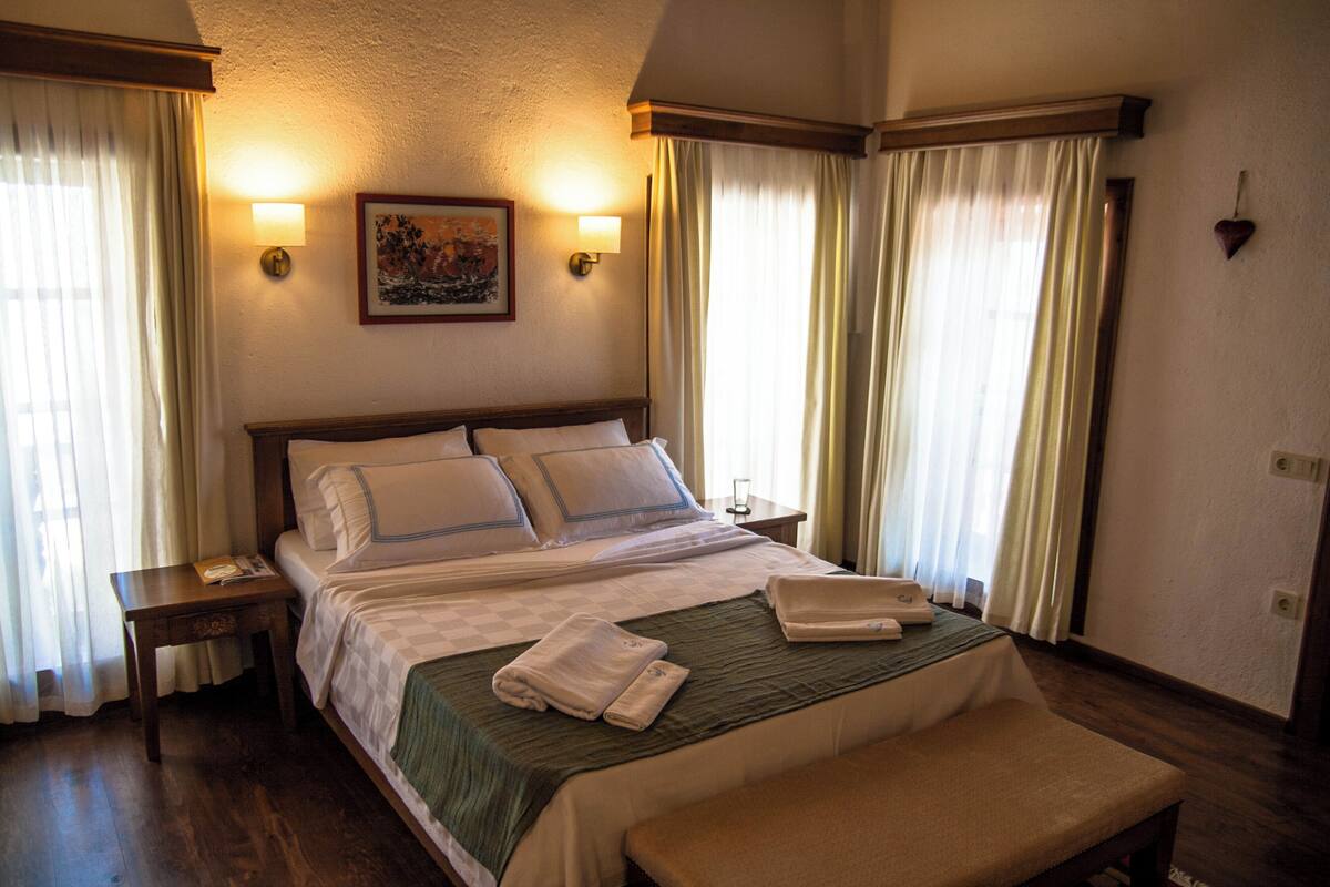 A hotel room with a large bed, two bedside tables, a bench, and a wall-mounted picture.