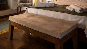 Habitación de hotel con techo de madera, cama con sábanas blancas, una silla, mesita de noche y chimenea.