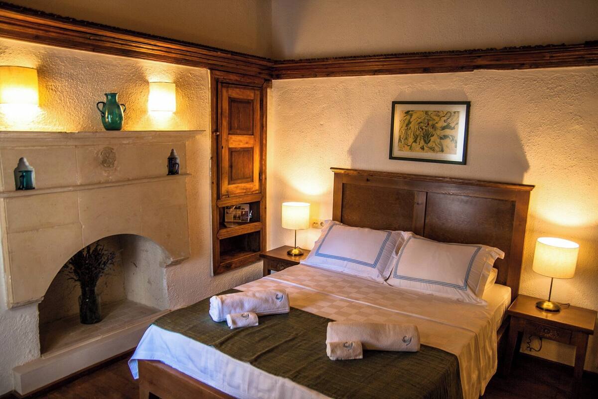 A neatly made bed with towels, a fireplace, and wall-mounted lamps.