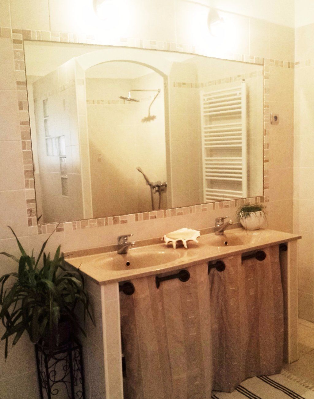 A bathroom with a large mirror, three sinks, a towel rack, and a potted plant.