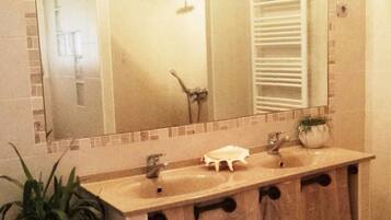 A bathroom with a large mirror, three sinks, a towel rack, and a potted plant.