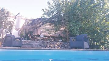 A pool area with lounge chairs, a stone wall, and a building with a thatched roof.