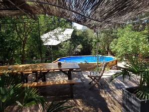 An outdoor pool area with a wooden table and chairs, surrounded by lush greenery.