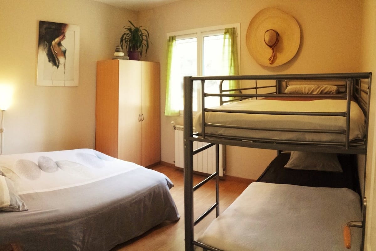 A room with bunk beds, a wardrobe, a painting, a hat on the wall, and a window with curtains.
