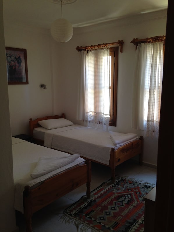 A bedroom with two single beds, a wooden headboard, a patterned rug, and a window with sheer curtains. - The White House Kalkan (Kas)