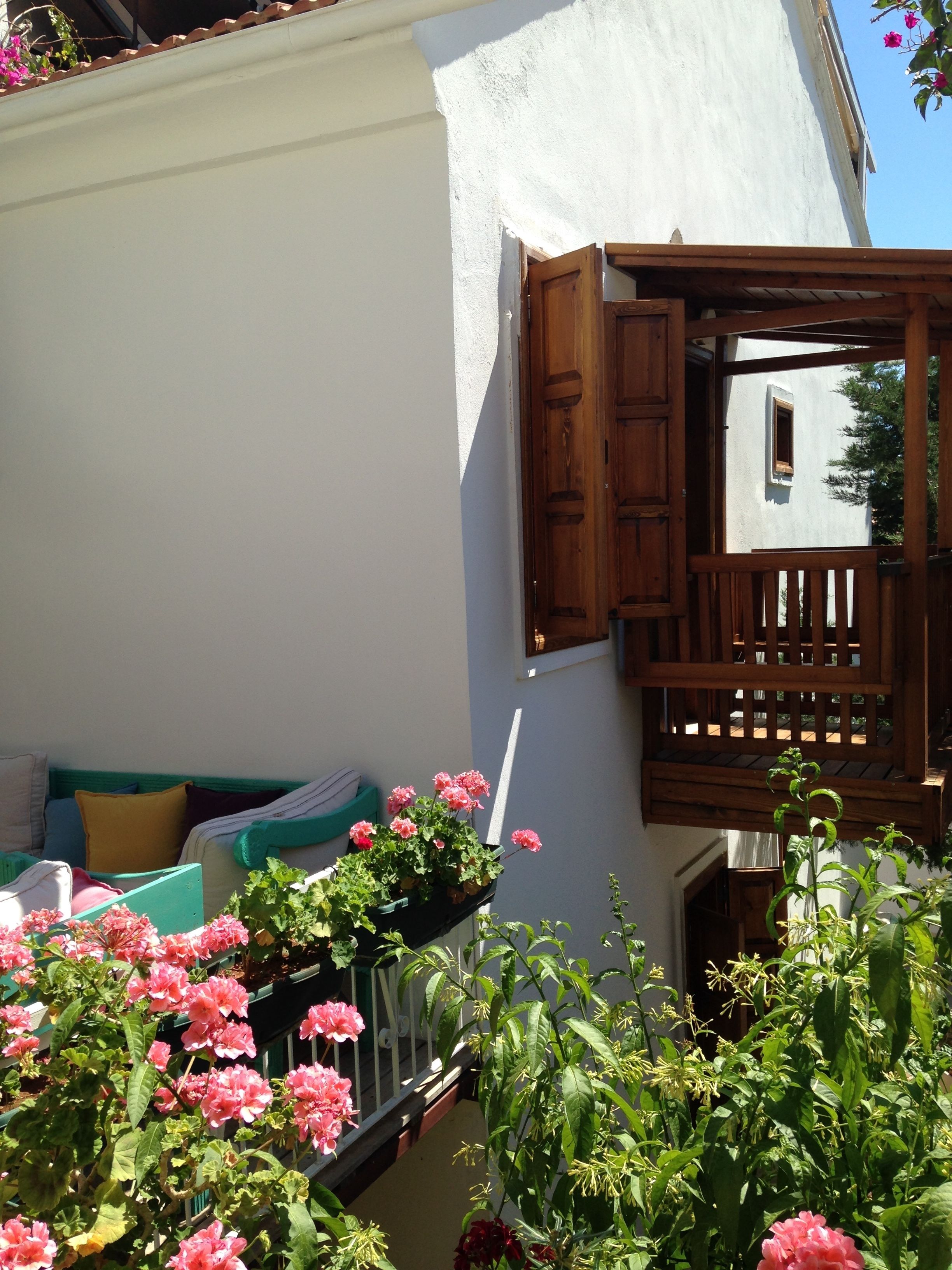 A balcony with a wooden railing, a white wall, and pink flowers in the foreground.