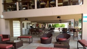 A spacious outdoor seating area with wicker furniture and red cushions, a bar area in the background, and a view of the greenery outside. - Flat Angra dos Reis Portogalo (Angra dos Reis)