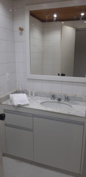 A bathroom with a white tiled wall, a large mirror, a sink with a towel, and a wooden ceiling. - Flat Angra dos Reis Portogalo (Angra dos Reis)
