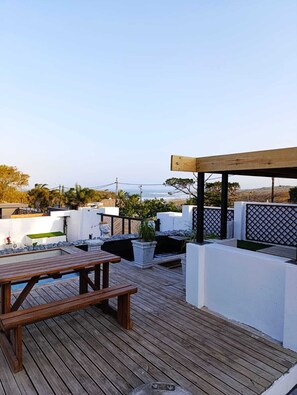 A rooftop patio with a wooden table, potted plants, and a pergola. - Reef View BnB (East London)