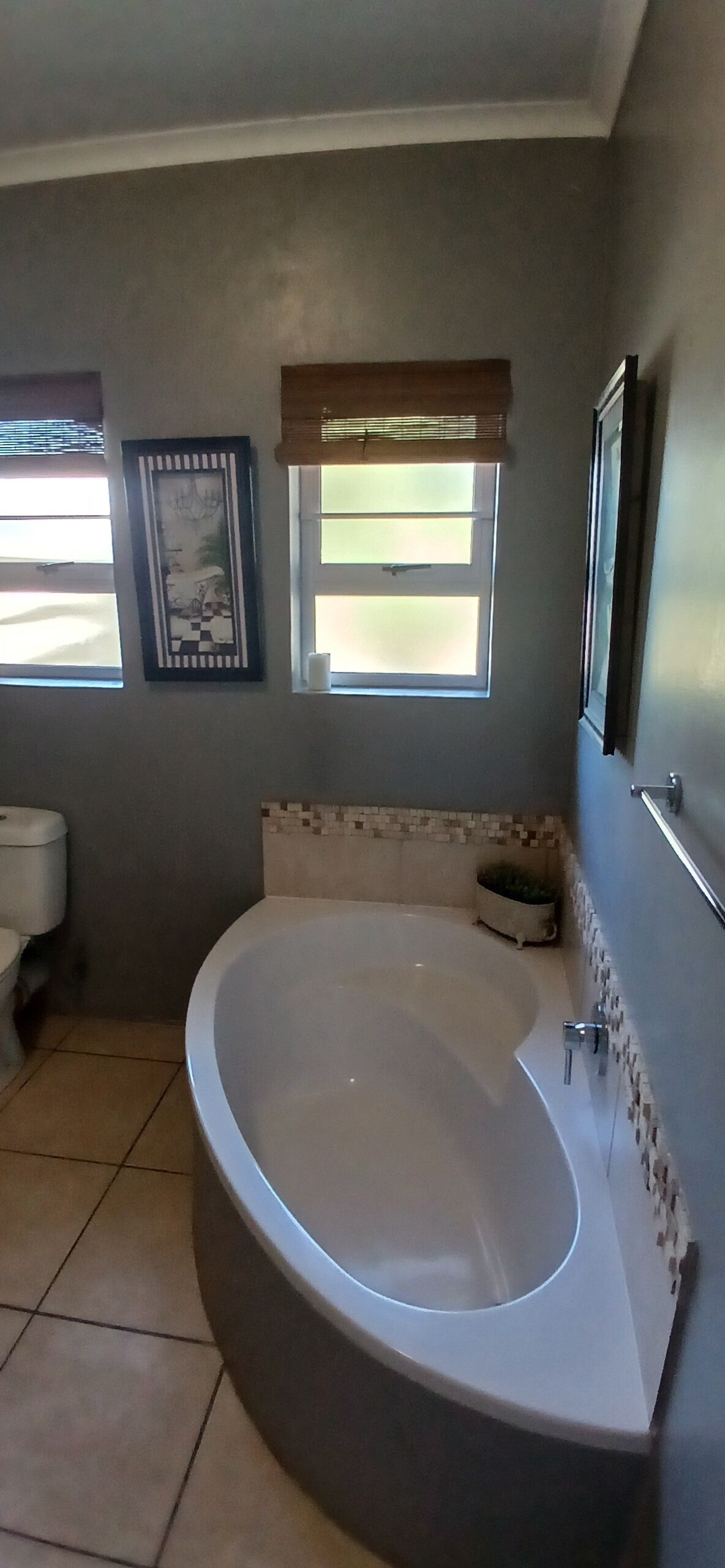 Un baño con una bañera grande, un inodoro, una ventana con persianas y un cuadro en la pared.