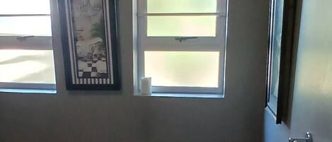 Un baño con una bañera grande, un inodoro, una ventana con persianas y un cuadro en la pared.