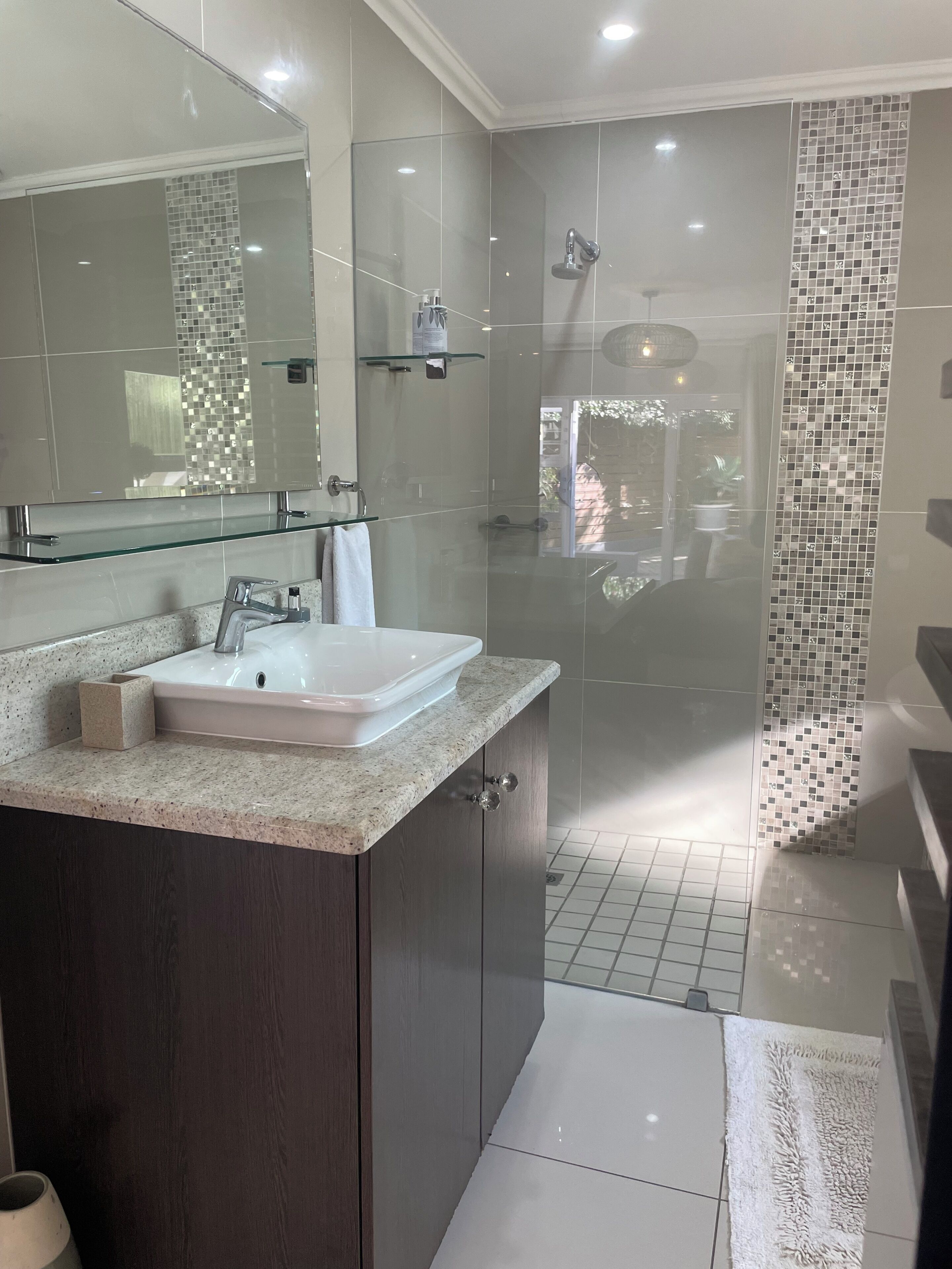 Un baño moderno con cabina de ducha de vidrio, un espejo grande y encimera de granito.