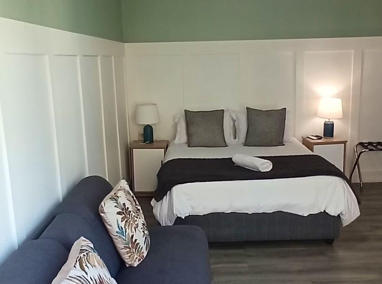 A bedroom with a bed, two bedside tables, a nightstand, a lamp, a sofa, and a pillow.