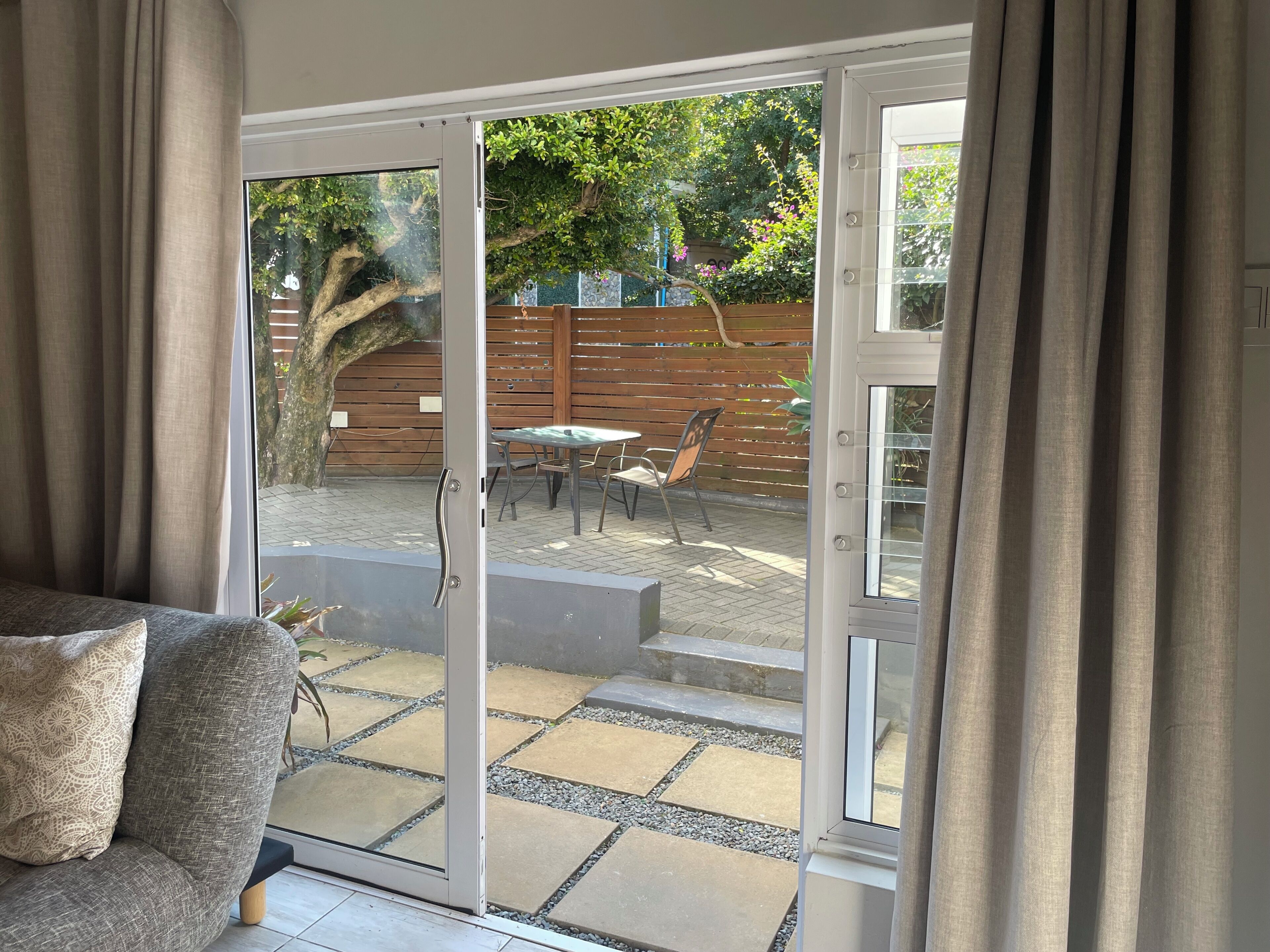 A room with a sliding glass door leading to an outdoor patio area with a table and chairs, a wooden fence, and a tree.
