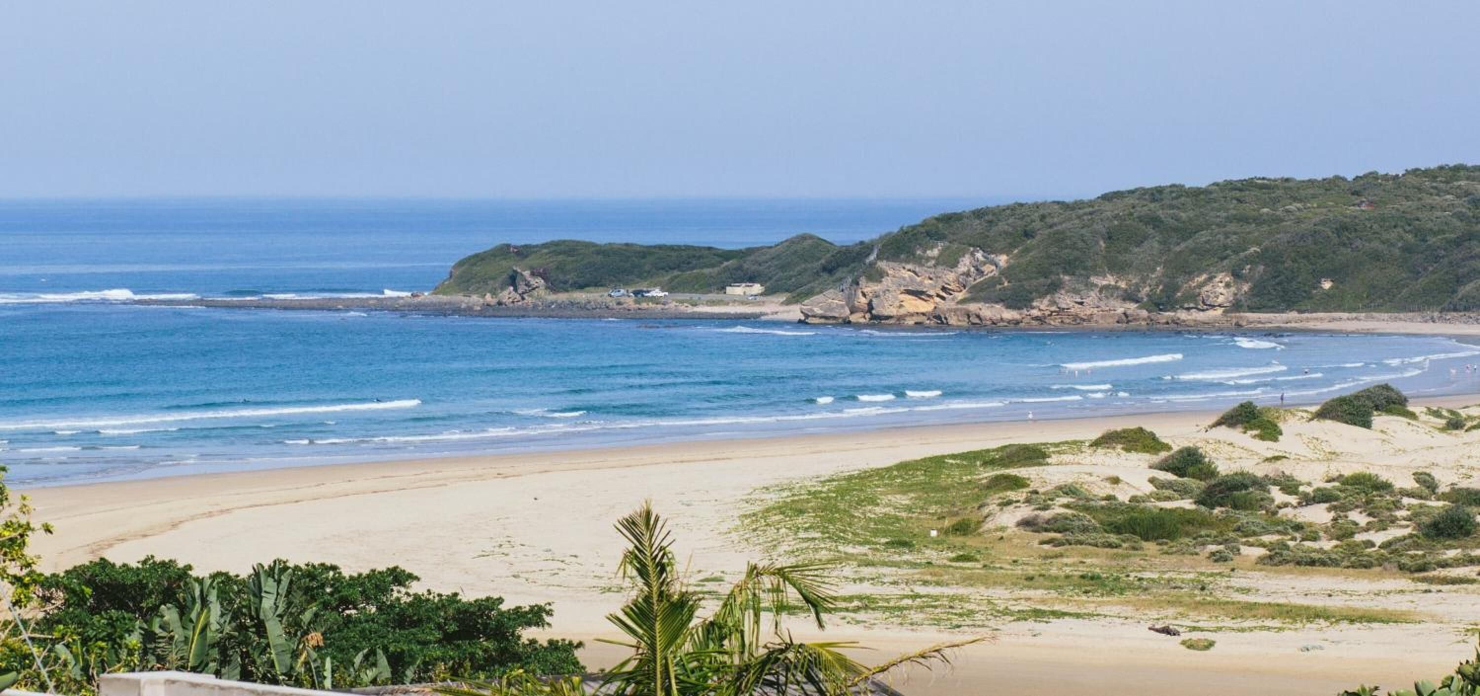 A beach with clear blue water, sandy shores, and green hills in the background.