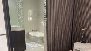 Une chambre à coucher moderne avec un grand lit, une table de chevet, une commode et une salle de bain visible à travers une porte en verre.