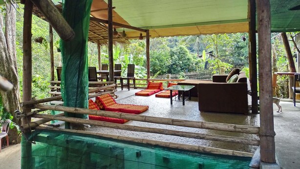 An outdoor seating area with a pool, wooden furniture, and a thatched roof structure. - Hill Tribe Art House (Chiang Rai)