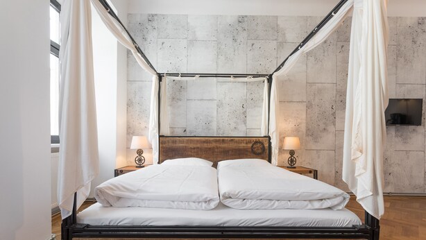 A bed with a wooden frame and white bedding, two bedside tables with lamps, and a stone wall in the background.