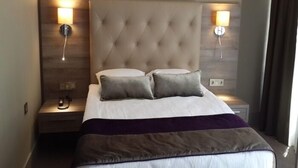 A hotel room with a tufted headboard, two bedside lamps, a bed with white linens and a purple throw, and a nightstand with a phone and a lamp. - Reda Palas Karanfil (Ankara)