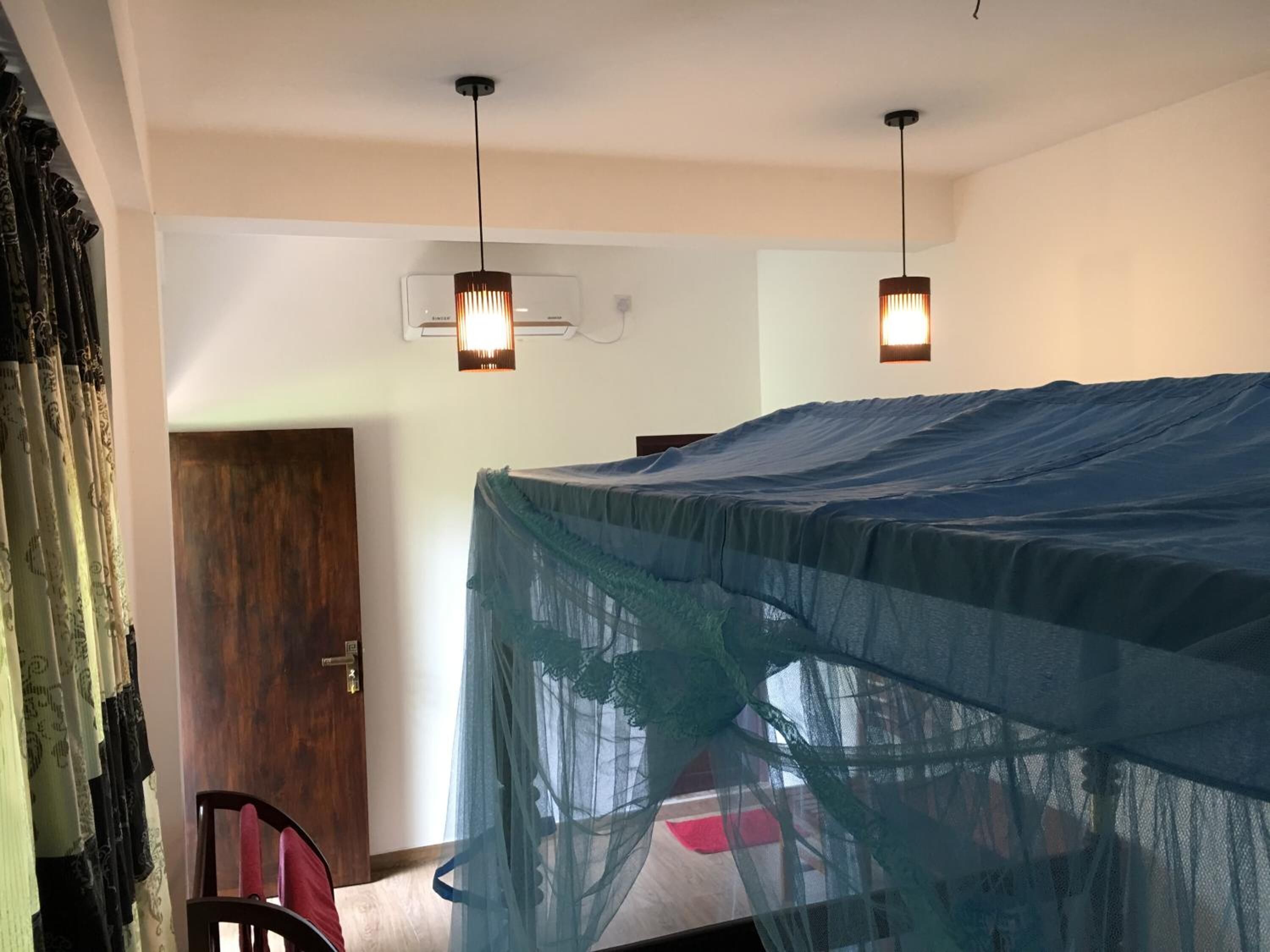 Un dormitorio con una cama cubierta con una tela de mosquitero azul, dos lámparas colgantes, una puerta de madera y una silla.