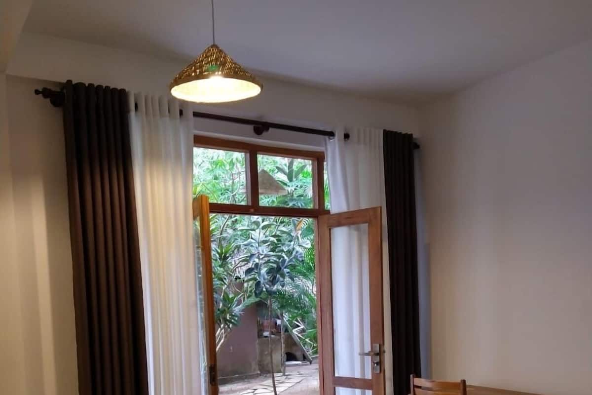 A room with a bed, a desk, and a view of a garden through an open door.