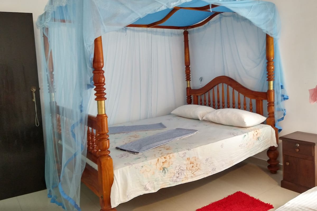 A bed with a wooden frame, a floral bedspread, and a blue mosquito net.