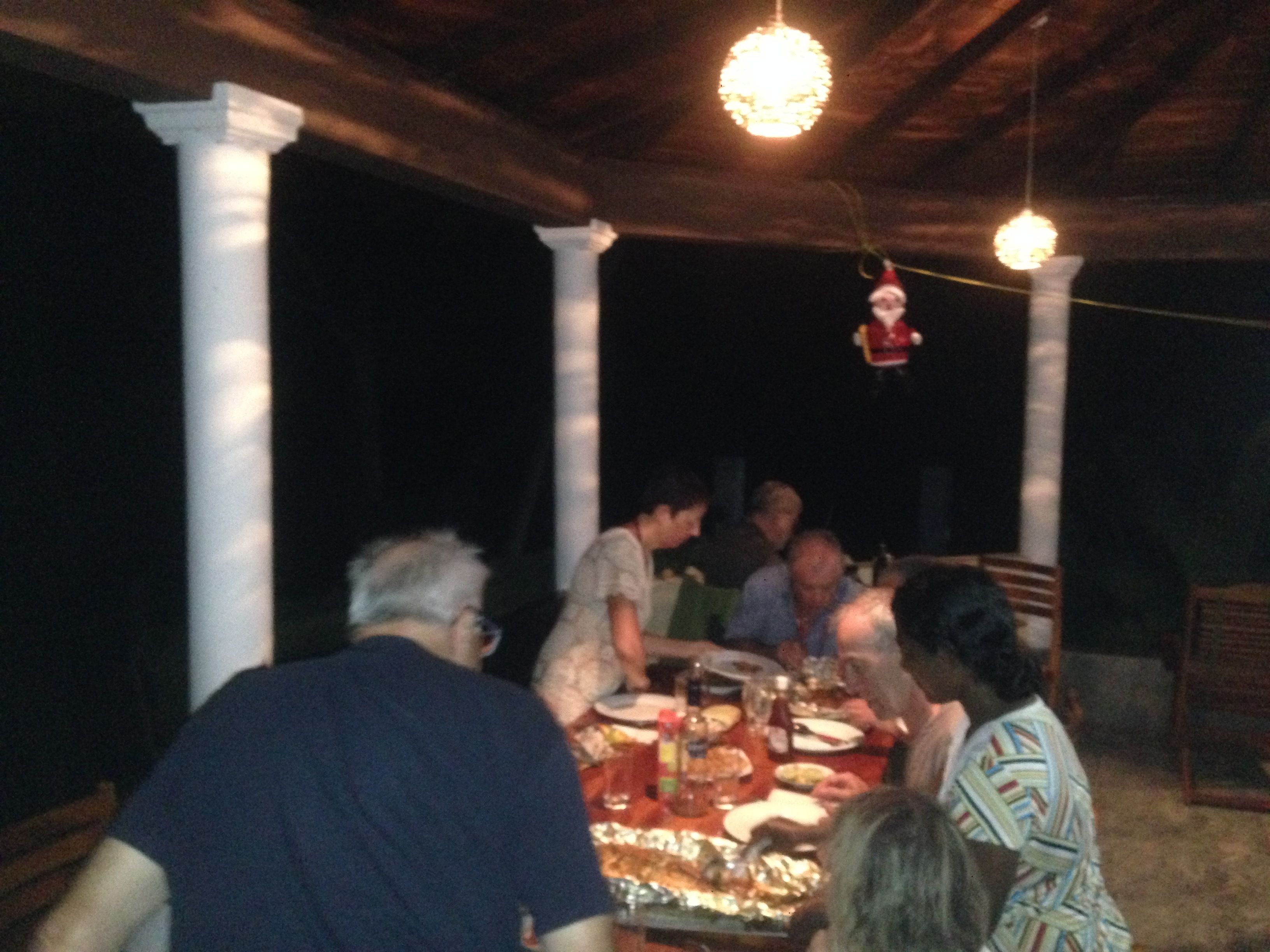 A group of people dining at an outdoor table with a chandelier overhead.