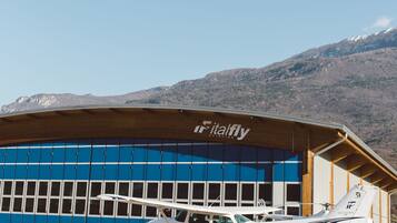 Un bâtiment sur lequel on peut lire l’inscription « Fitalfly », avec un petit avion portant le nom « I-MMCA » garé devant.