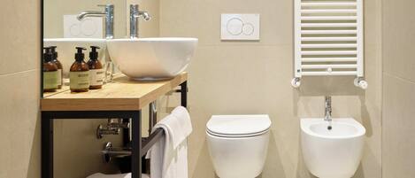 A modern bathroom with a large mirror, a vessel sink, two bidets, and a towel rack.