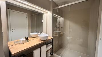 Un baño moderno con dos lavabos, cabina de ducha de vidrio y tocador de madera.