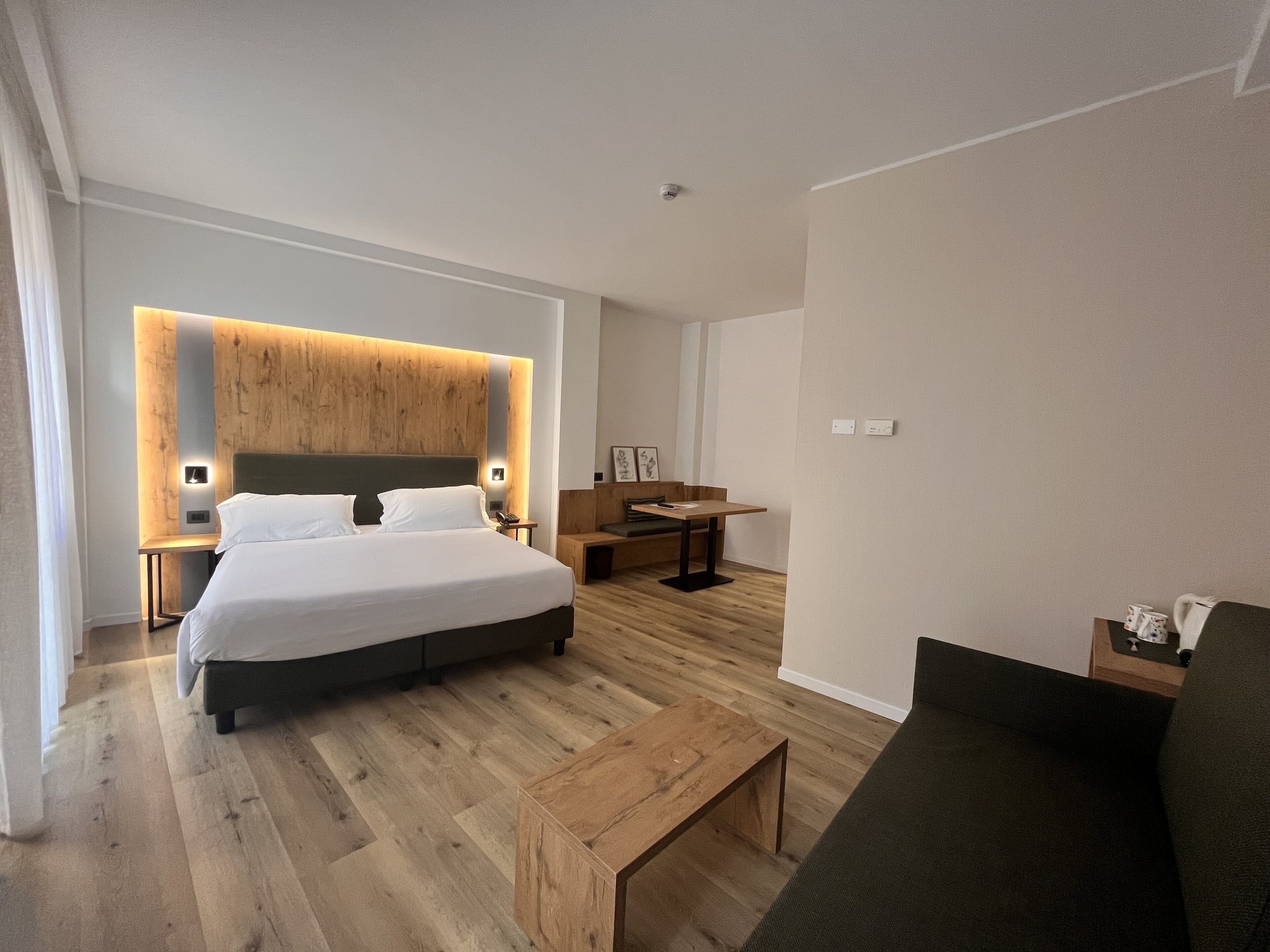 Une chambre d’hôtel moderne avec un grand lit, un mur décoratif en bois, un bureau et un canapé.