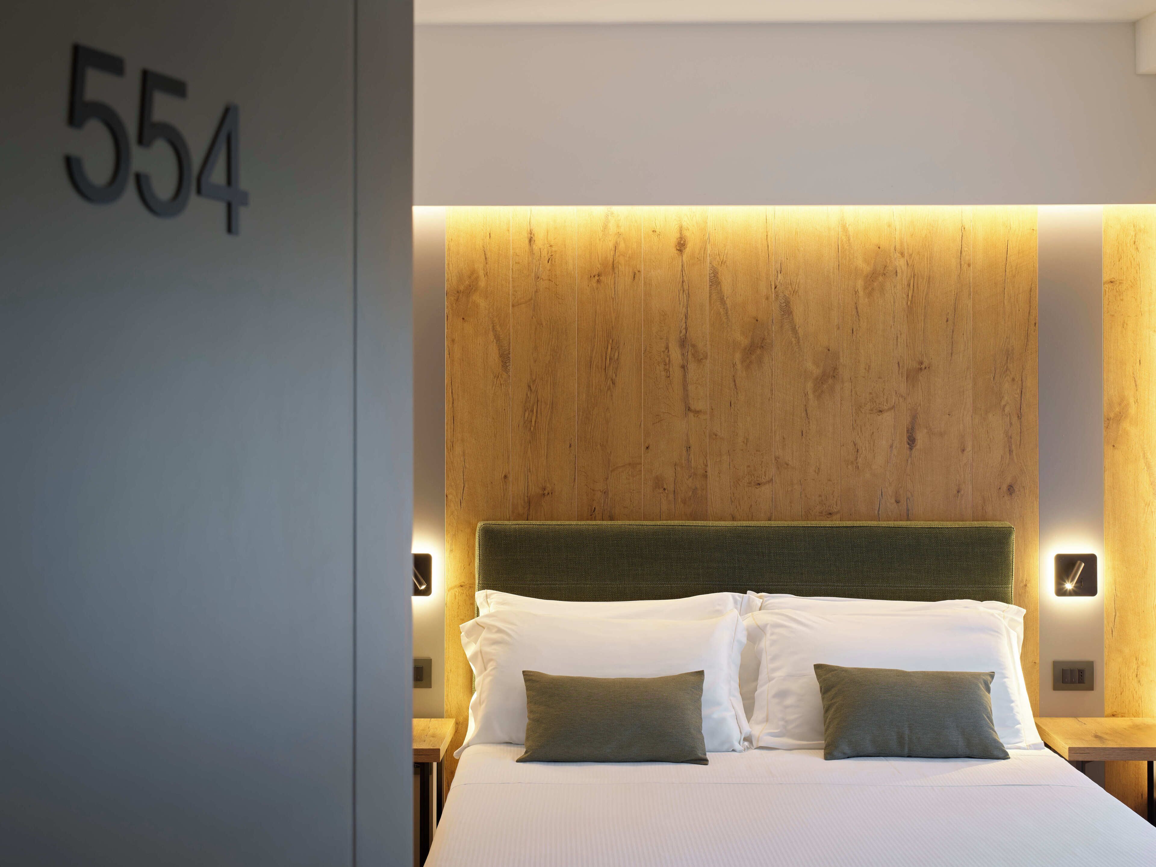 Habitación de hotel con una cama grande, cabecero de madera y el número '554' en la pared.