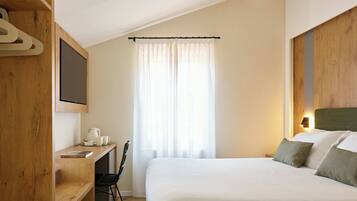 Ein Hotelzimmer mit Bett, Schreibtisch mit Stuhl, einer Kaffeemaschine und einem Fernseher an der Wand.