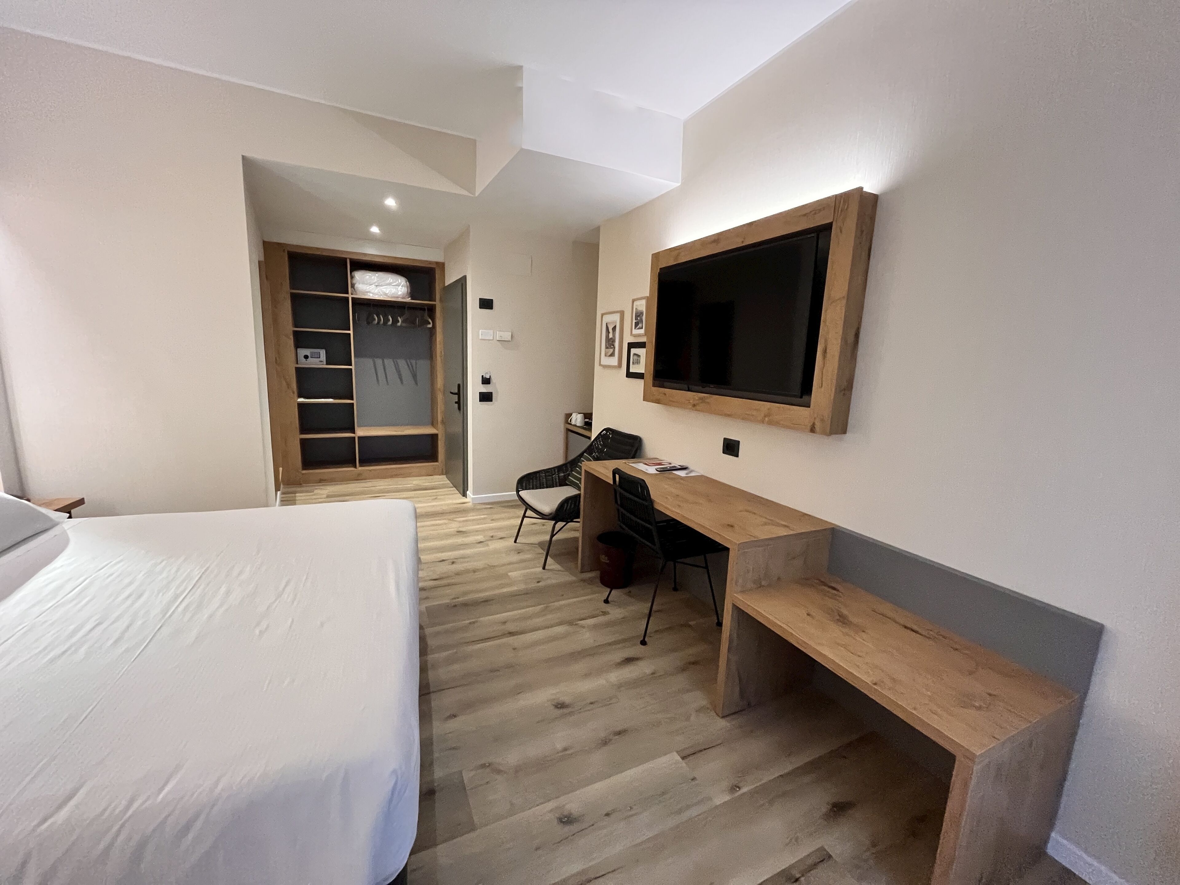 A hotel room with a bed, a desk, a chair, a TV, and a wardrobe.