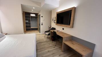 A hotel room with a bed, a desk, a chair, a TV, and a wardrobe.